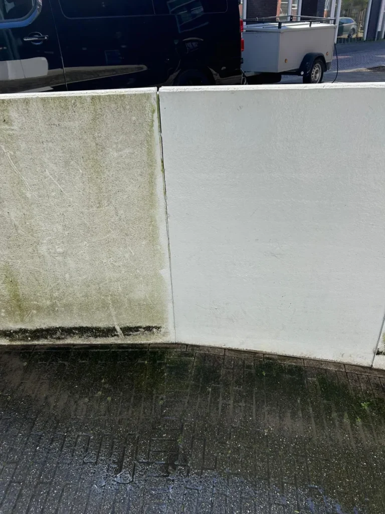 Betonnen muur half schoongespoten: links nog groene aanslag, rechts weer wit