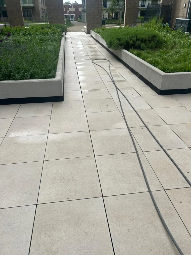 Binnenplaats van een appartementencomplex wordt schoongespoten, slangen over de tegels