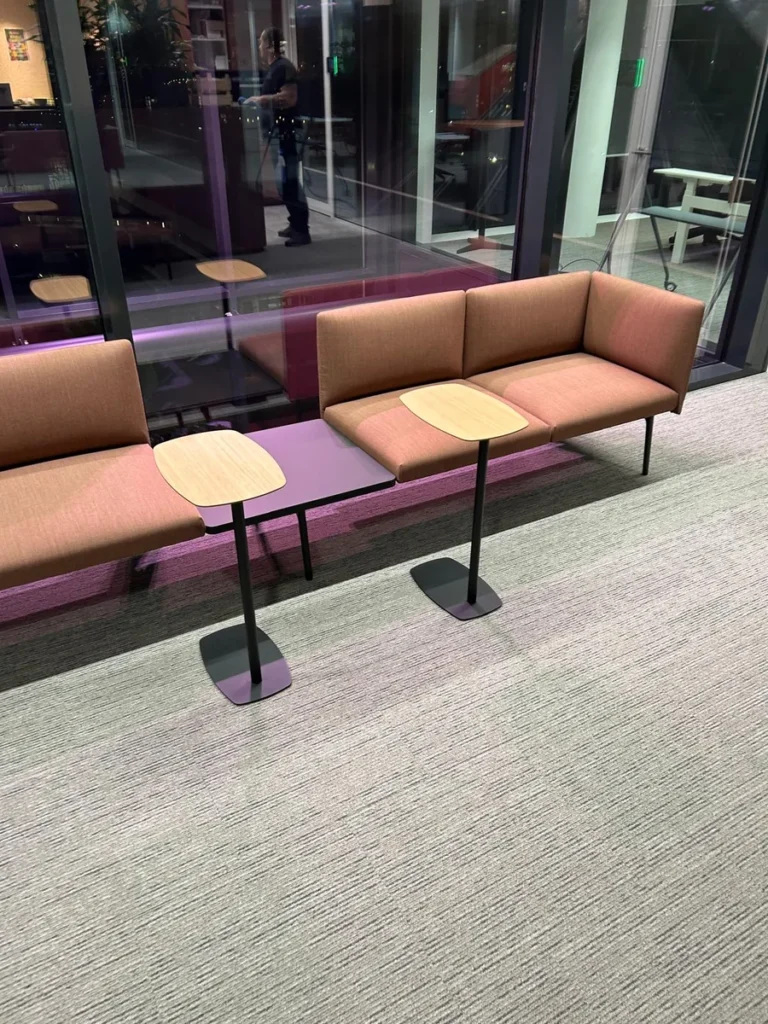 Schoongemaakte lounge met zitbanken en tafeltjes achter een glazen wand