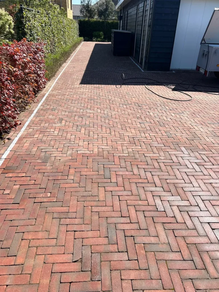 Schoongemaakte klinkerbestrating langs een groenstrook achter een pand